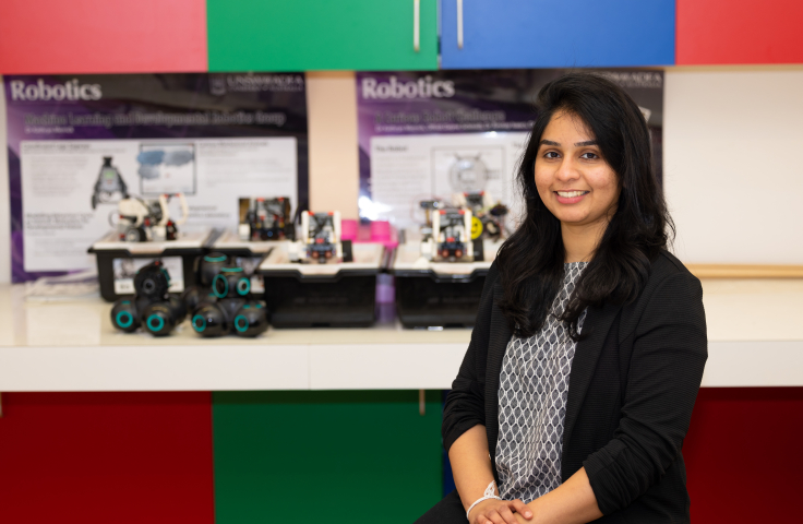 Dr Dilini Samarasinghe sits in a colourful lab with robots in the background.