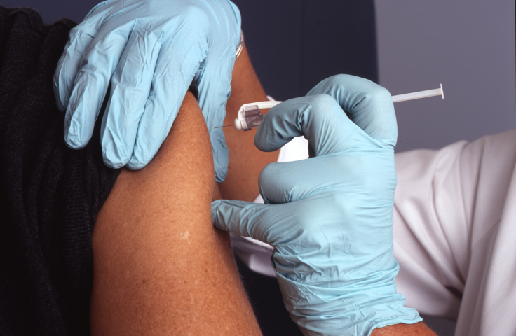 A close-up of a medical professional wearing disposable gloves injecting the COVID-19 vaccine into an arm.