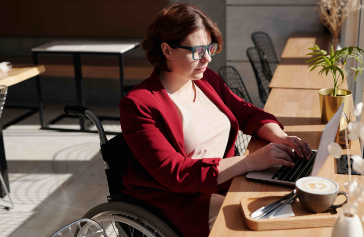 A woman sits in a wheelchair with laptop and coffee